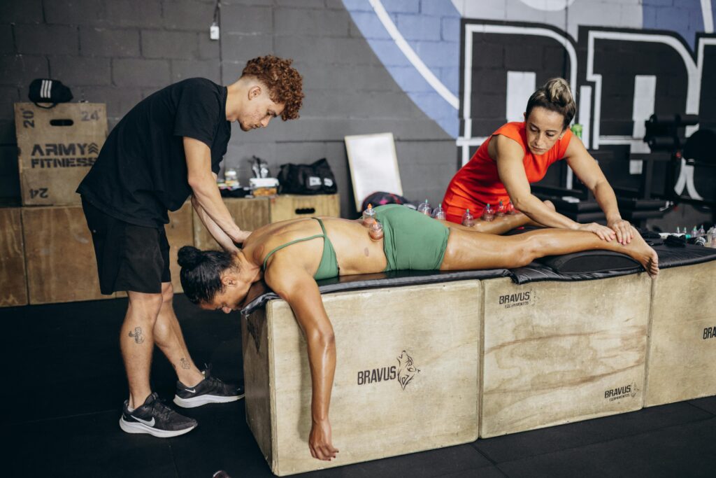 Athlete receives cupping therapy for muscle recovery in a gym setting with two therapists.