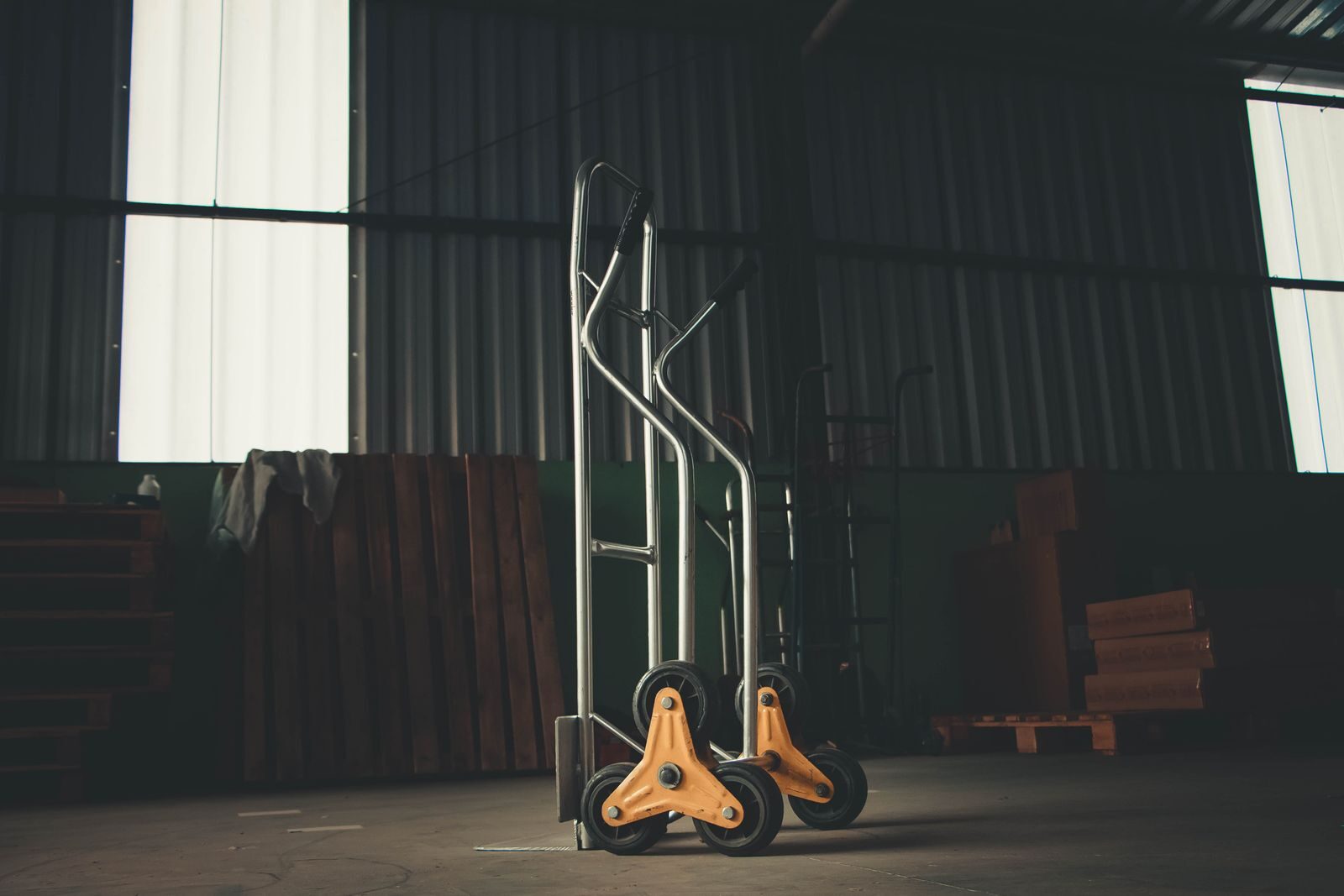 A metal hand truck stands ready for use in a dimly lit warehouse. Ideal for storage and transport imagery.