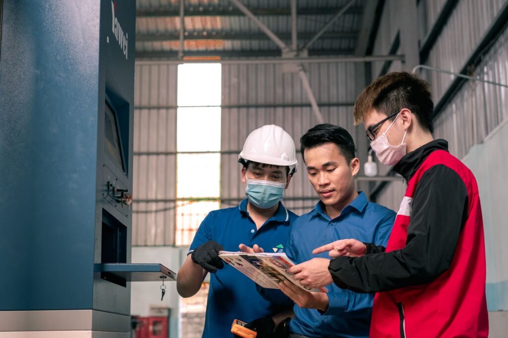 Workers in a warehouse reviewing blueprints, emphasizing teamwork and safety.