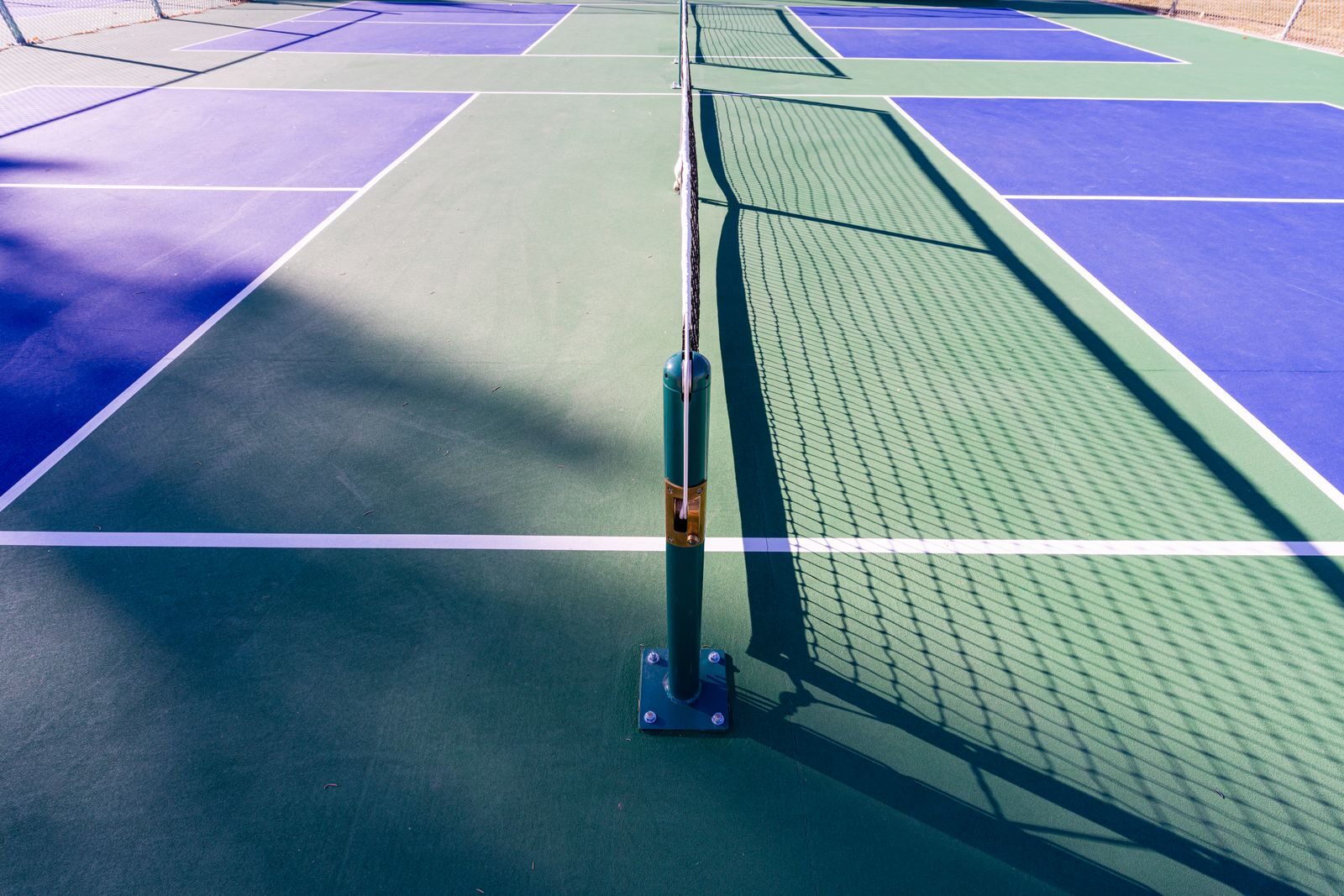 A pickleball court with blue and green surfaces under sunlight, showcasing the net and court lines.