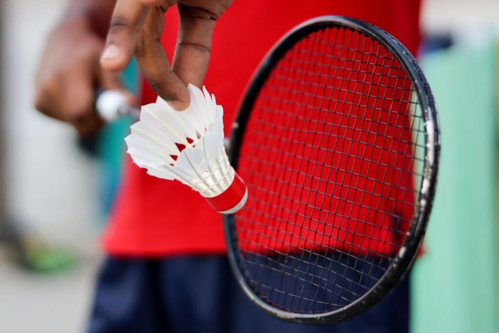 A detailed view of a hand holding a badminton shuttlecock and racket, ready to play.