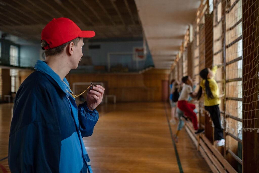 A coach guides young students during a physical education session in an indoor gym.