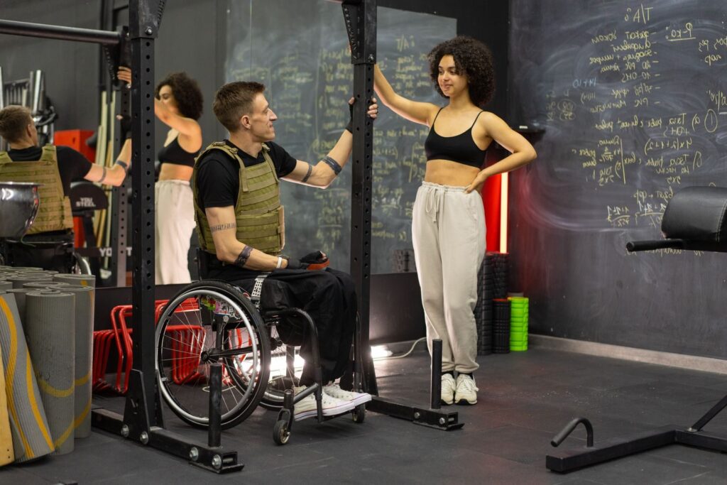 A man in a wheelchair engages in fitness training with a coach in a gym.