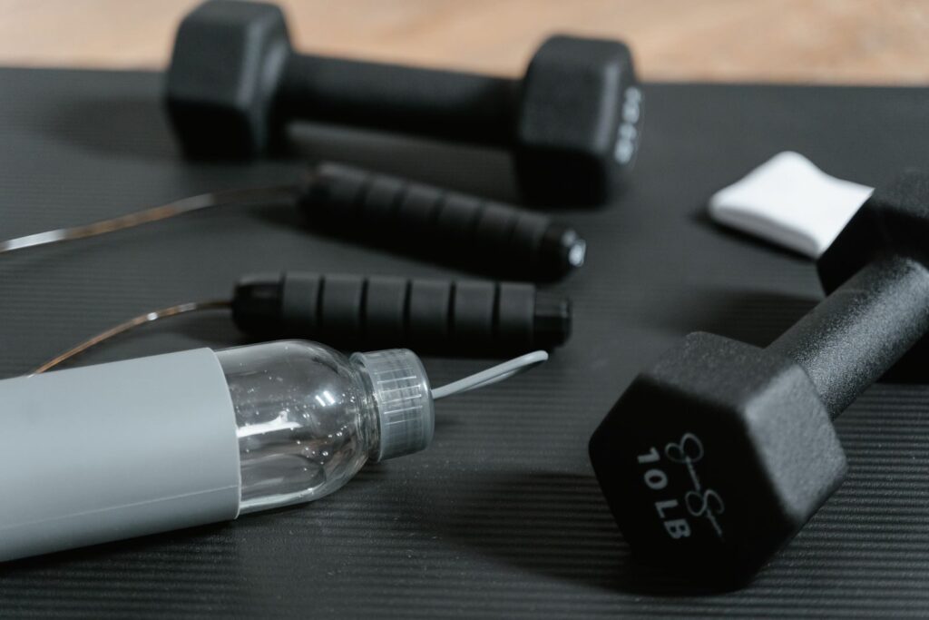 Close-up of gym essentials: dumbbells, jump rope, and water bottle on a mat.