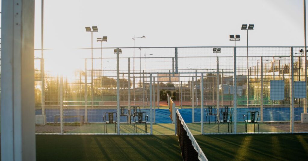 A scenic view of an outdoor tennis court with fences and lighting at sunset, ideal for sports or recreation themes.