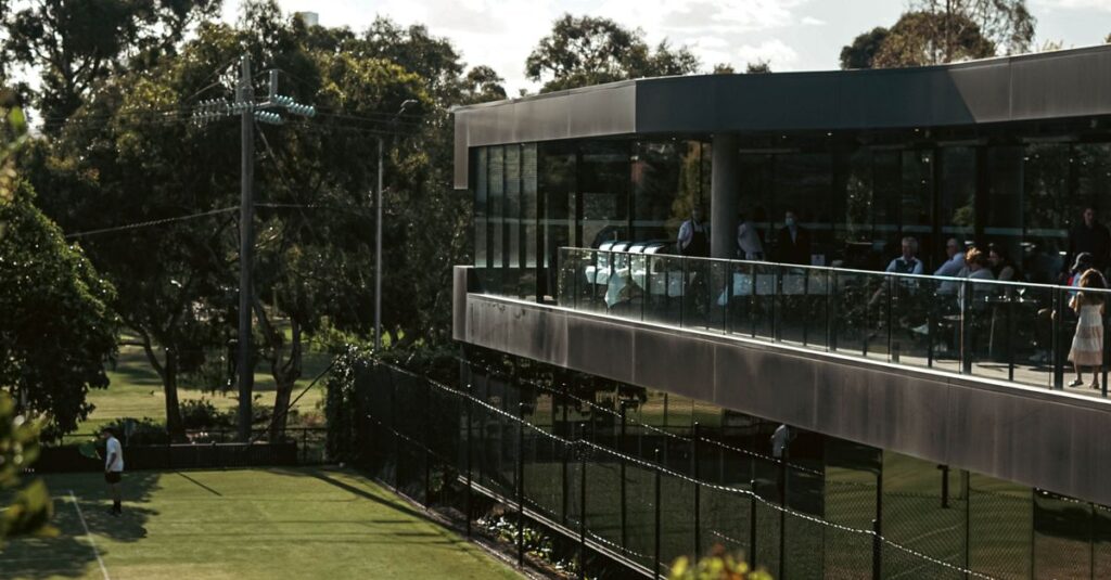 Beautiful outdoor tennis court next to a modern clubhouse under a clear blue sky.