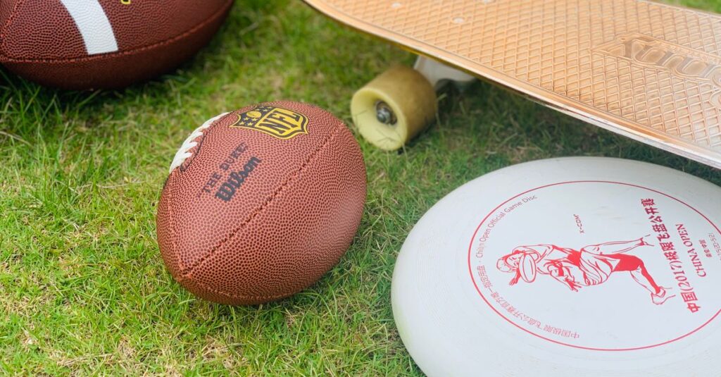 A close-up of sports equipment including a football, skateboard, and frisbee on grass.