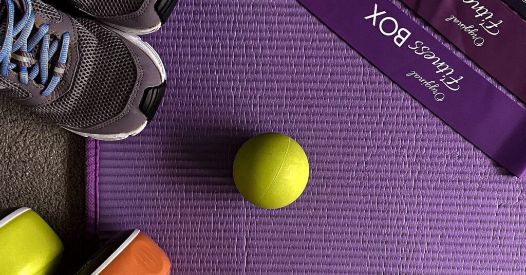 Flat lay of gym shoes, resistance bands, dumbbells on a fitness mat.