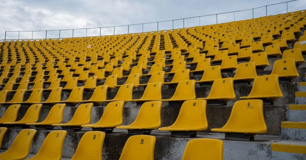 View of empty yellow seats arranged in rows at a stadium on a cloudy day.