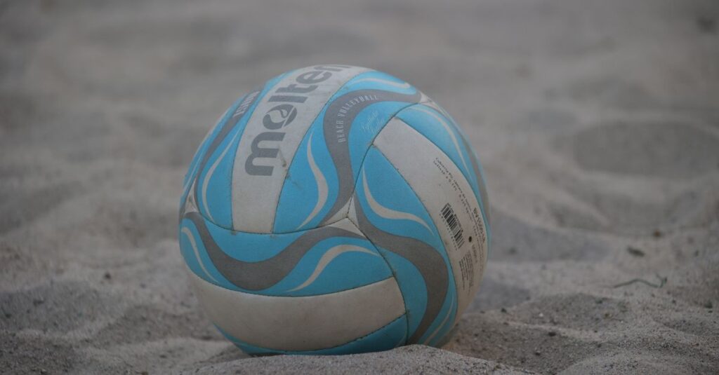A close-up of a colorful beach volleyball resting on sand.