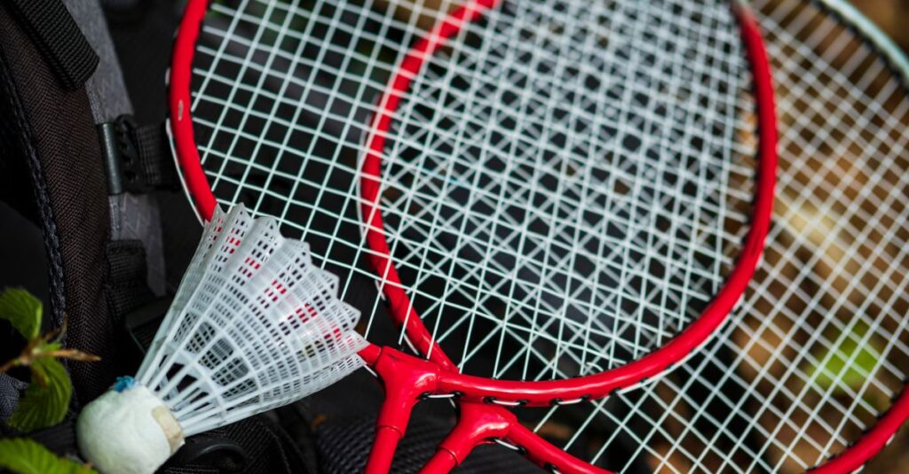 Two red badminton rackets and a shuttlecock on a backpack outdoors, perfect for leisure and sports activities.
