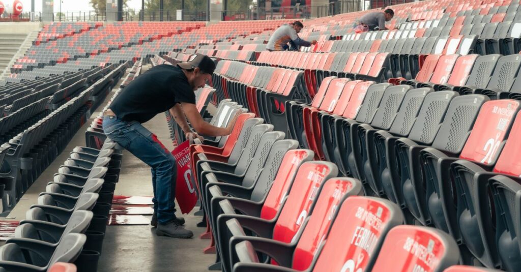 Workers preparing stadium seating for an upcoming sports event, organizing and cleaning rows of seats.