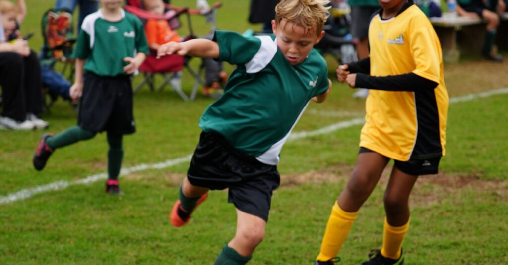 Boys and girls in team soccer jerseys playing soccer on a green field outdoors.