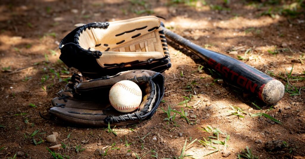 Close-up of baseball equipment including ball, bat, and gloves on a rural dirt ground.