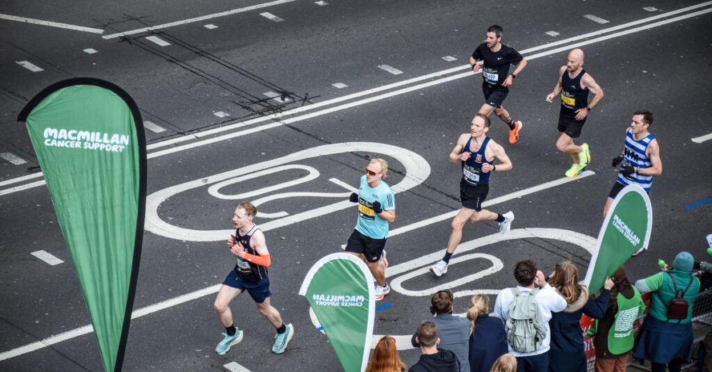 Runners participating in a marathon on London streets, viewed from above, with spectators cheering.