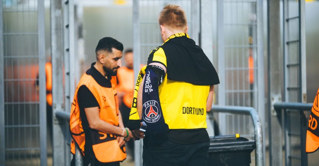 Security personnel and a fan at a football stadium checkpoint in Dortmund, Germany.
