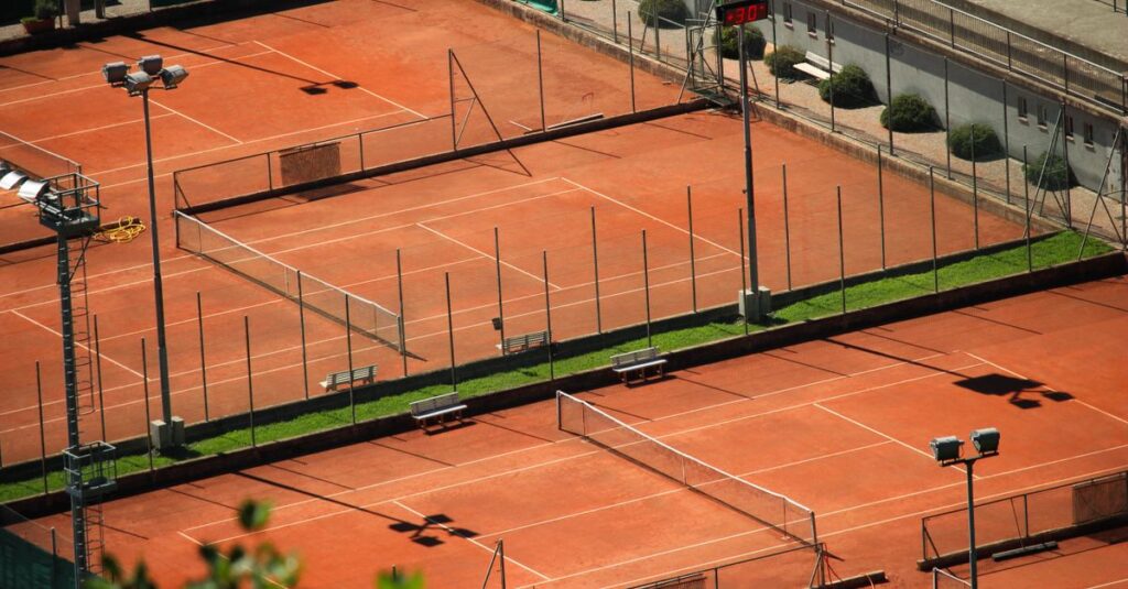 Aerial shot of empty red clay tennis courts on a sunny day with shadows.