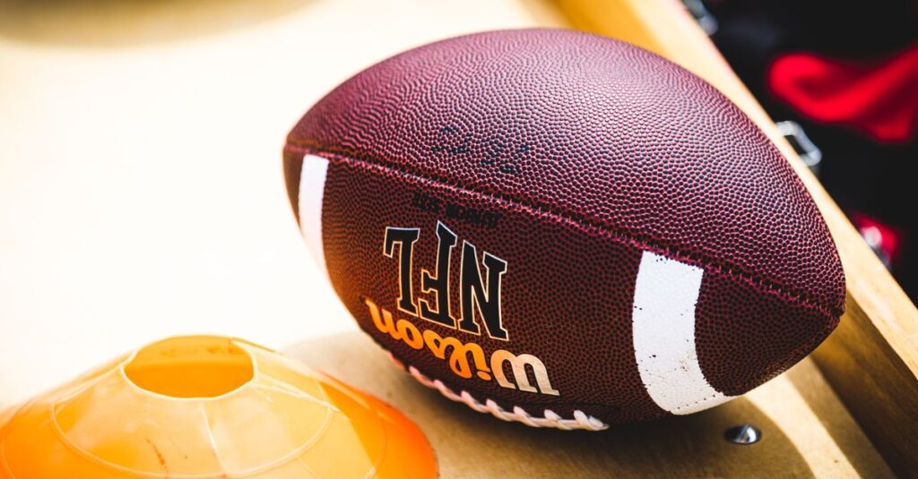 An American football placed on a training bench next to an orange training cone, ideal for sports concept.