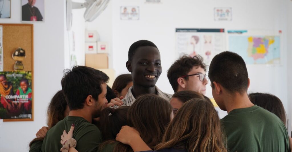 A diverse group of young adults share a group hug indoors in a classroom setting, promoting unity and friendship.