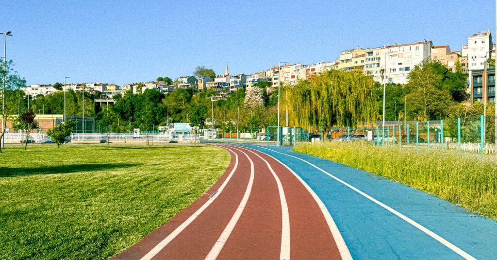 A vibrant running track winding through a green park with cityscape background, under a clear blue sky.