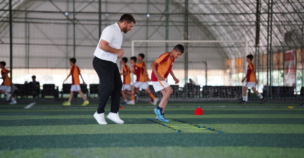 A young boy trains under a coach in a structured soccer practice indoors.