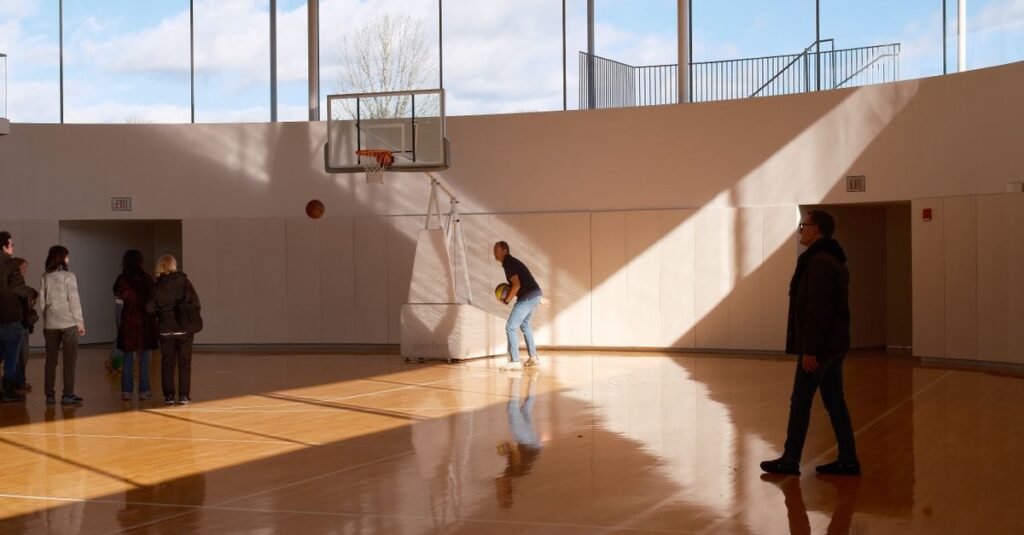 Spacious indoor basketball court with people under a wooden ceiling and natural light.