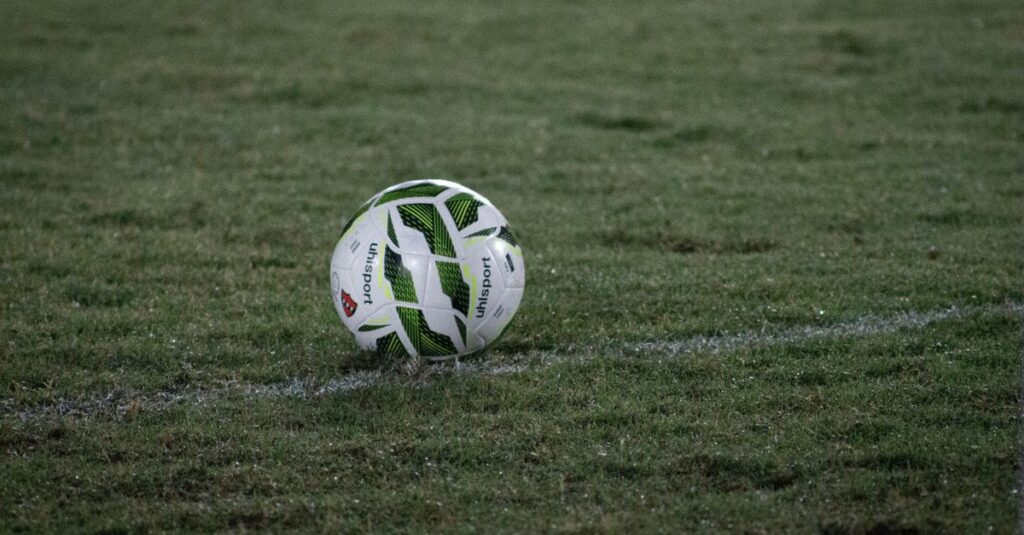 A soccer ball resting on a grass field, captured during nightfall with visible dew.