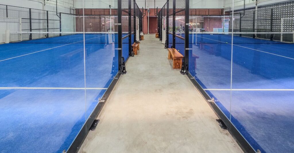Modern indoor padel tennis courts featuring bright blue surfaces and glass partitions.