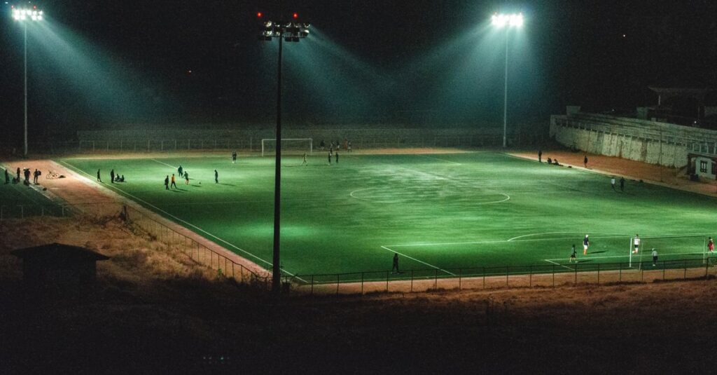 A vibrant nighttime soccer match in an illuminated stadium in Paro, Bhutan, captured from an elevated angle.