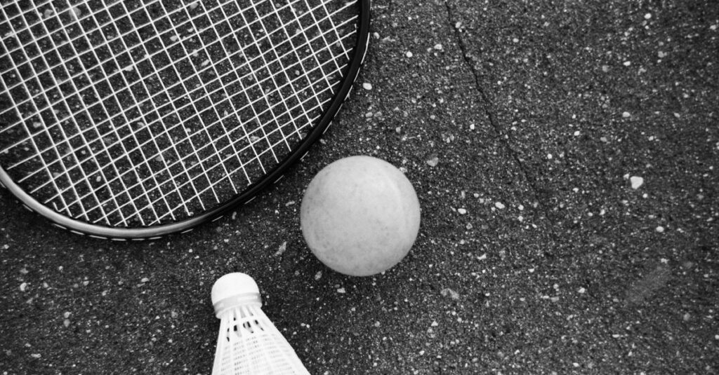 From above of black and white tennis racket with ball and shuttlecock placed on asphalt ground
