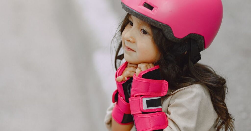 Young girl wearing a bright pink helmet and gloves, providing a side view with a blurred background.