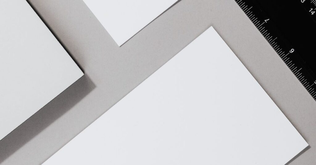 Flat lay of blank paper sheets and ruler on a gray background, ideal for office themes.