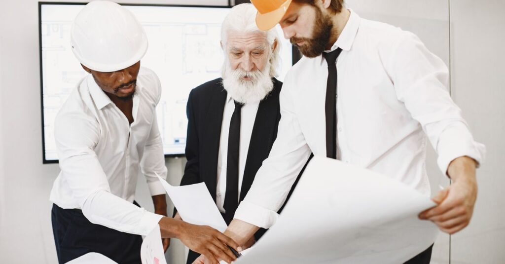 Three architects in office reviewing blueprints, showcasing teamwork and professional attire.