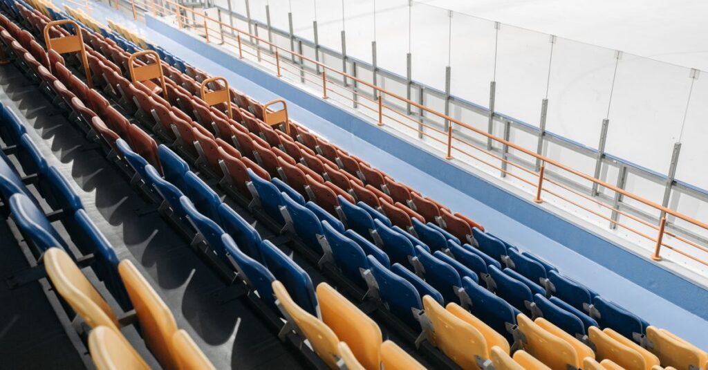 An empty stadium with multicolored seats overlooking an ice skating rink.
