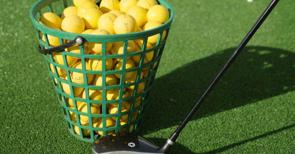 A close-up of a basket full of yellow golf balls with a golf club on green turf, ideal for sports imagery.