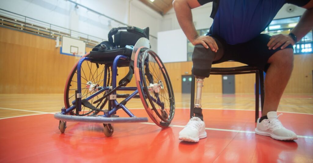 A focused shot of an adaptive athlete with a prosthetic leg taking a break on a basketball court indoors.