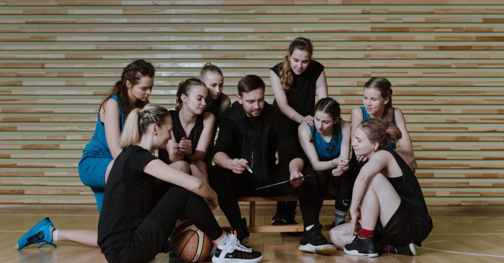 A coach strategizes with a women's basketball team in a gymnasium.