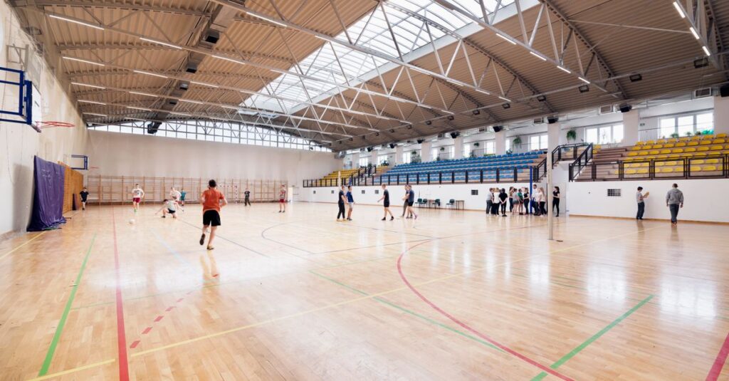 Wide-angle view of an indoor basketball court with players practicing and engaging in sports activities.