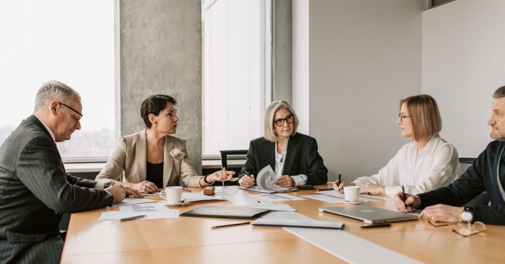 Five business professionals engaged in a meeting in a modern office setting, discussing documents and ideas.