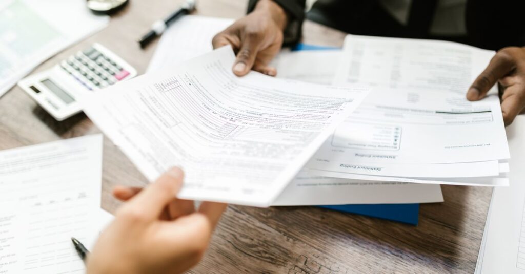 Two professionals exchanging documents in an office setting, focusing on paperwork and data analysis.