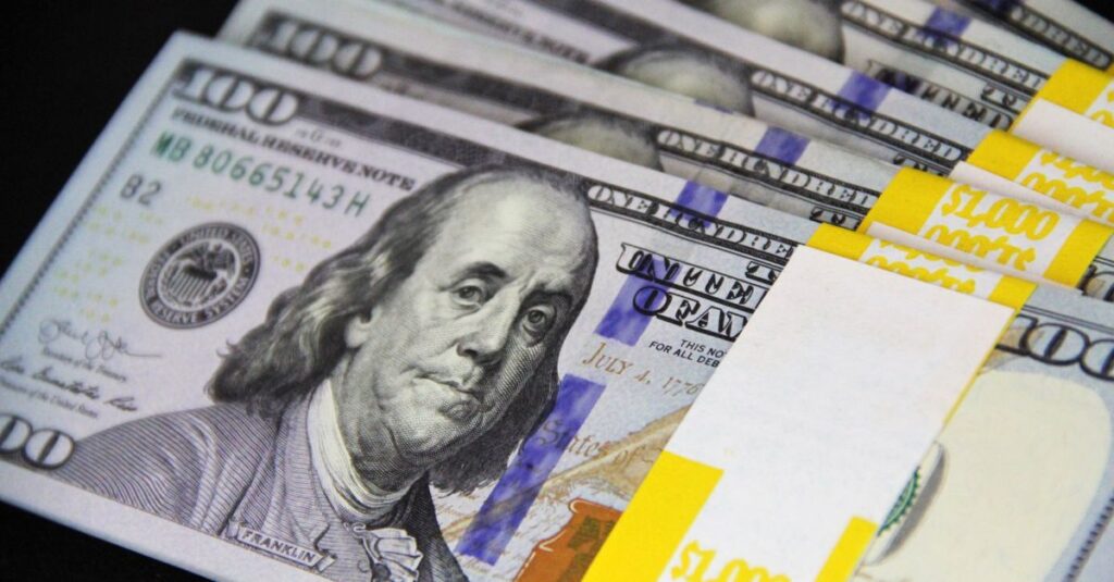 Close-up of stacked US hundred dollar bills on black surface, emphasizing wealth and finance.