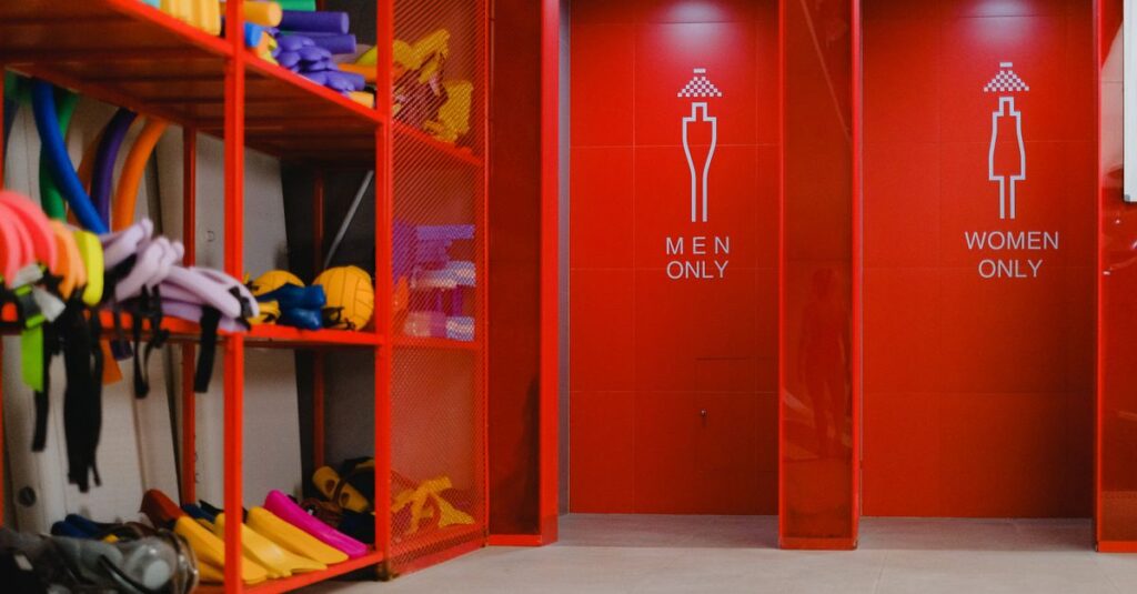 Colorful pool gear in storage beside gender-specific showers with vibrant red decor.