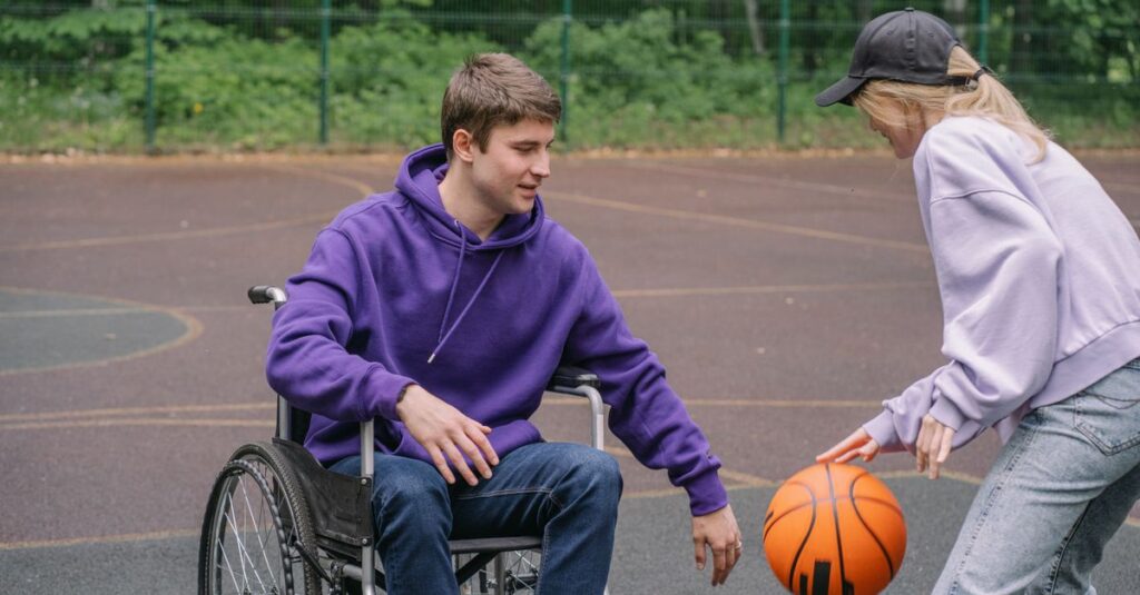 A man in a wheelchair plays basketball outdoors with a friend, promoting inclusion and sports.