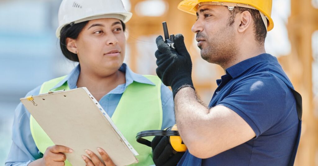 Two construction workers in safety gear discussing plans at a construction site.