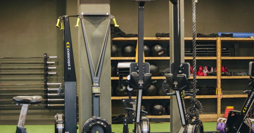 Modern gym with exercise equipment including rowing and ski machines, weights, and ropes.