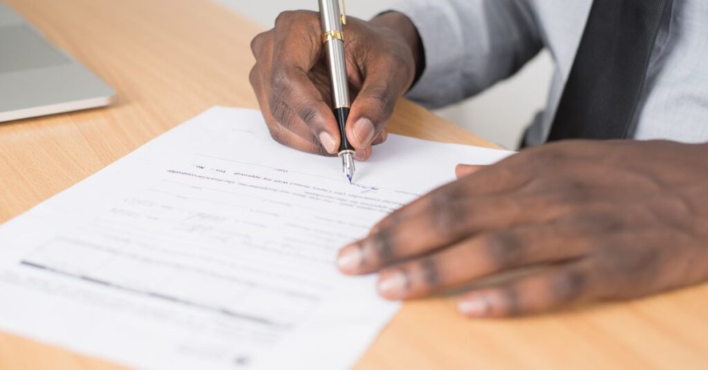 Close-up of a businessman signing a contract at an office desk.