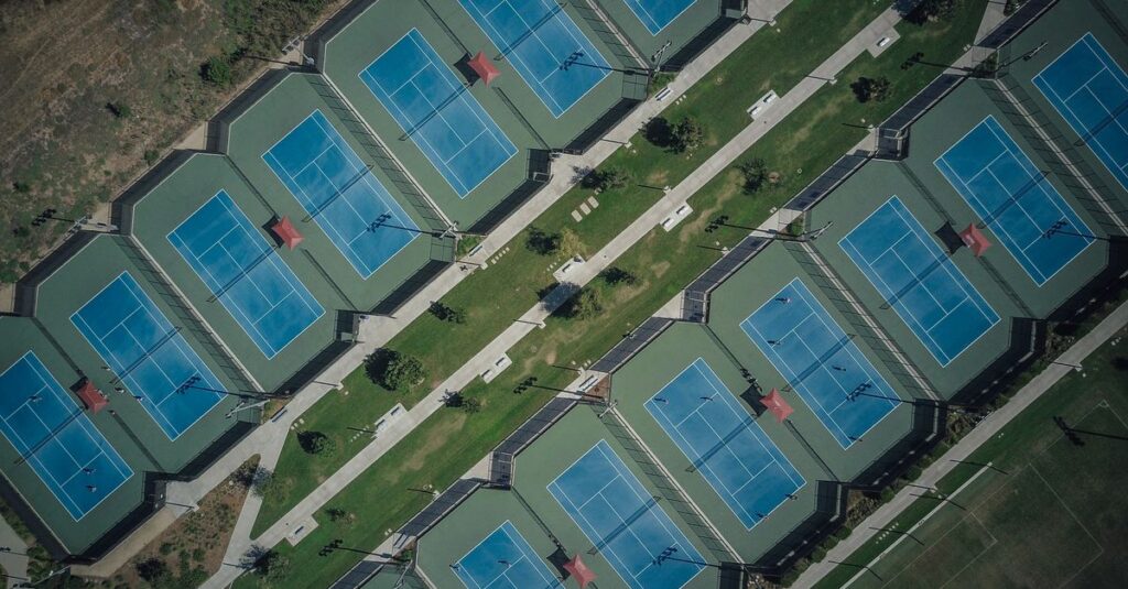 High-angle aerial shot of blue tennis courts in a geometric layout on a sunny day.