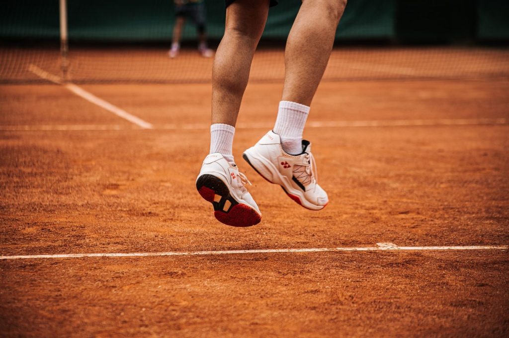 Low angle view of a tennis player jumping on a clay court, showcasing movement.