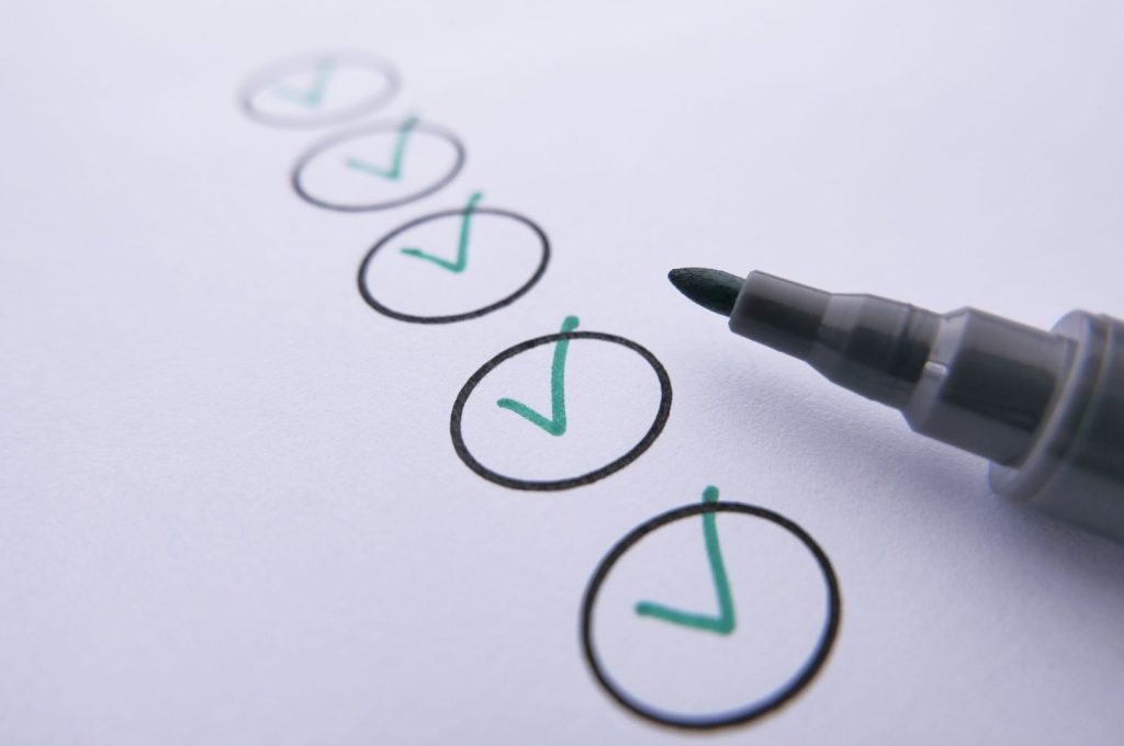 Close-up of a checklist with green checkmarks on white paper using a marker.