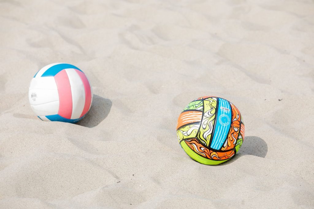 Two colorful balls resting on a sandy beach under the bright summer sun.
